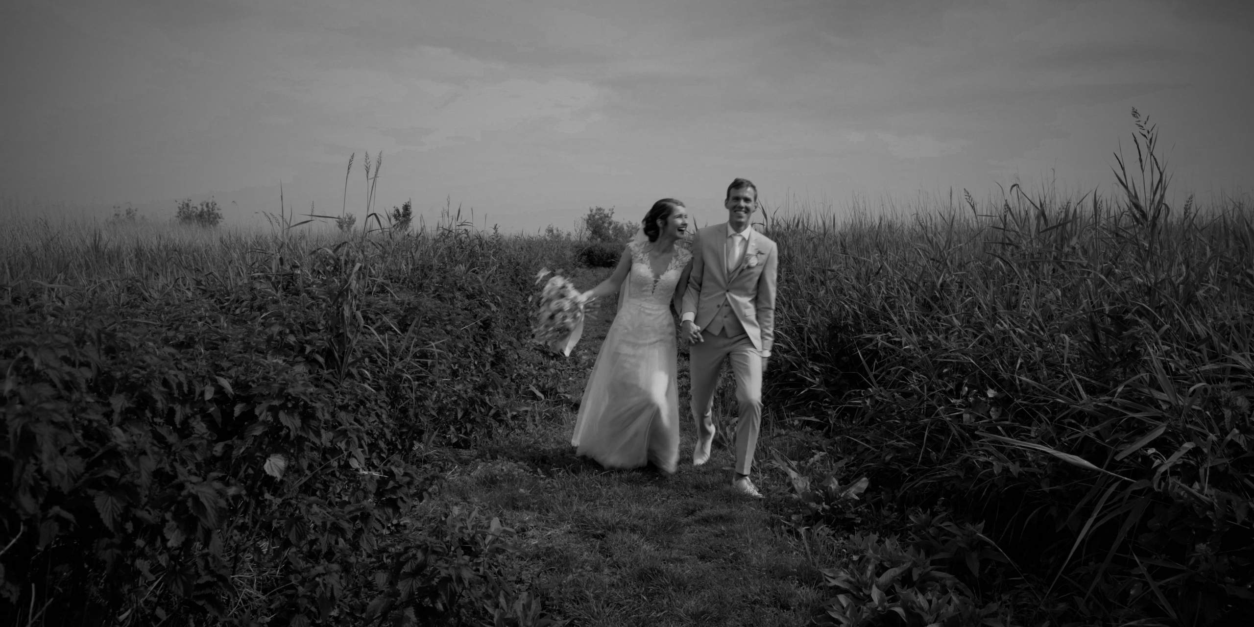 Sander en Lotte lopen hand in hand door het hoge gras, zwart-wit