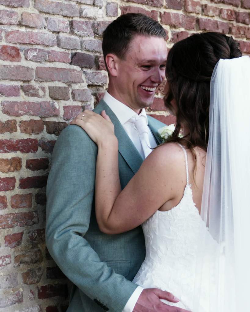 Wesley en Janieke lachend in een omhelzing tegen een oude bakstenen muur
