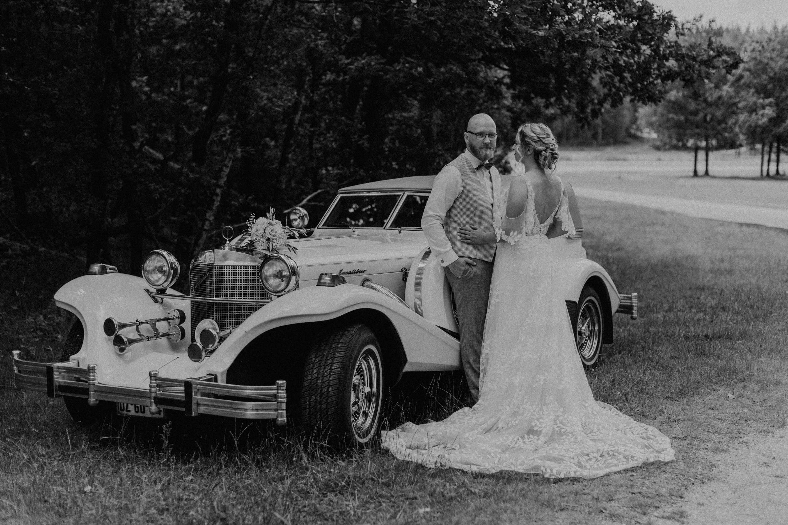 Gerwin en Elena bij een witte oldtimer als trouwauto, zwart-wit