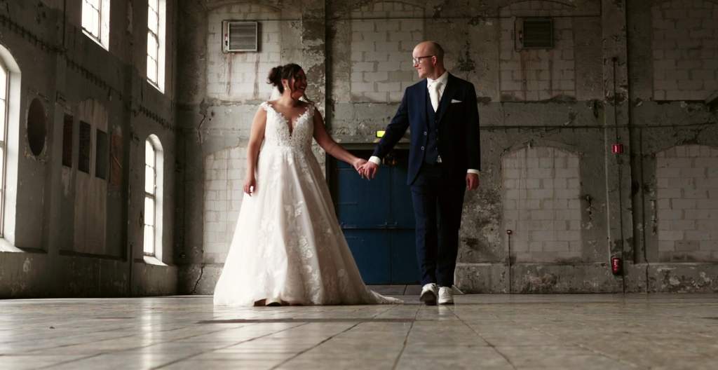 Thomas en Simone lopen hand in hand door een industriële hal op hun trouwdag in Groningen
